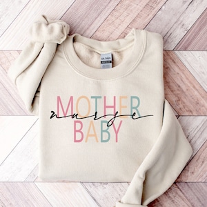 Puede incluir: Una sudadera beige con el texto "MOTHER" en naranja, "nurse" en rosa y "BABY" en azul y verde.