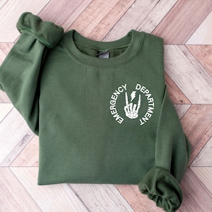 May include: A dark green sweatshirt with a white circle graphic that says "Emergency Department" with a skeleton hand making a peace sign and a lightning bolt.