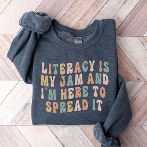 May include: A dark grey sweatshirt with the text "Literacy is my jam and I'm here to spread it" in colourful, retro-style lettering.