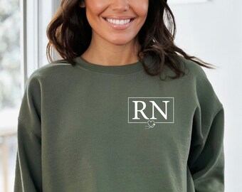 May include: A green sweatshirt with a white square on the front that says "RN" with a small heart and a stethoscope graphic below the text.