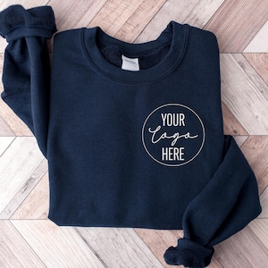 Peut inclure: Un sweat-shirt bleu marine avec un cercle blanc sur le devant qui dit "YOUR LOGO HERE" dans une police d'écriture manuscrite.