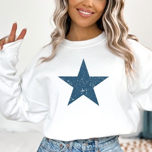 May include: White sweatshirt with a distressed blue star graphic.