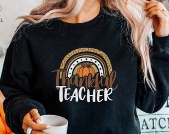 May include: A black sweatshirt with a rainbow design featuring a pumpkin and the text "Thankful Teacher".