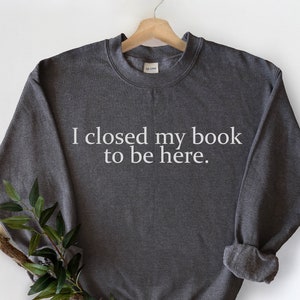 May include: A dark grey sweatshirt with the text "I closed my book to be here." printed in white on the front.