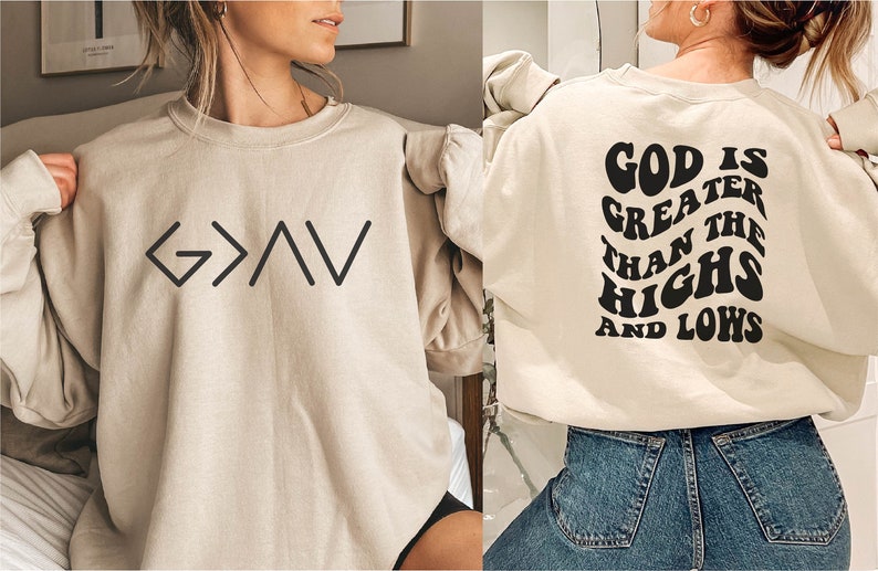 以下が含まれることがあります： 前面に「G>A>V」と黒で書かれたグラフィック、背面に「神は高みと低みよりも偉大である」と黒で書かれたグラフィックが施されたベージュのトレーナーです。