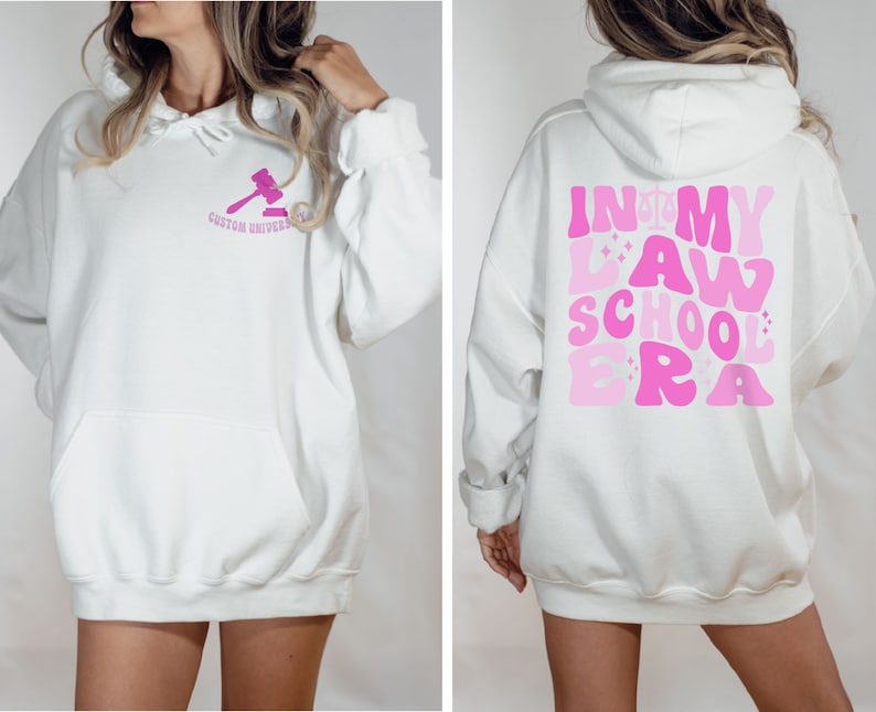 May include: White hoodie with a pink gavel graphic on the front and the text "In My Law School Era" in pink on the back.
