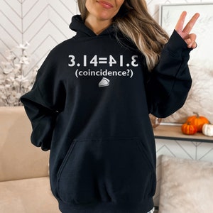 May include: Black hoodie with a white graphic that reads "3.14=&pi;.e (coincidence?)" and a small pie slice icon.