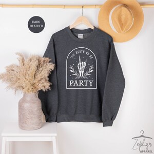 May include: Dark heather grey sweatshirt with a white graphic of a skeleton hand making a rock and roll sign. The graphic is inside a white arch with the text "Til Death Do Us Party".