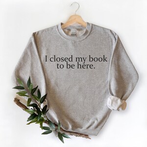 May include: A grey sweatshirt with the text "I closed my book to be here." printed on the front.