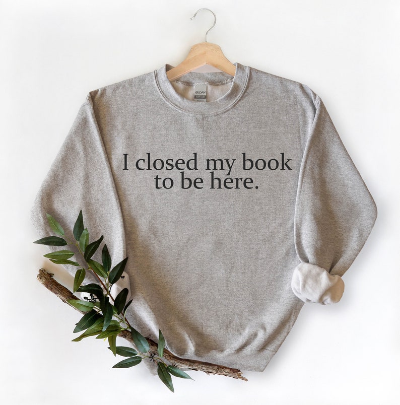 May include: A grey sweatshirt with the text "I closed my book to be here." printed on the front.