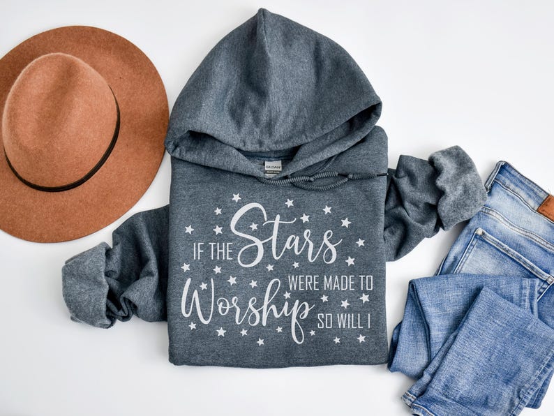 May include: A gray hooded sweatshirt with the text "If the Stars Were Made to Worship So Will I" in white, surrounded by stars. A brown hat and blue jeans are also in the image.