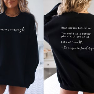 May include: Black sweatshirt with the text "you are enough" on the front and "Dear person behind me: The world is a better place with you in it. Lots of love - the person in front of you" on the back.