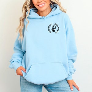 May include: A light blue hoodie with a black graphic of a skeleton hand making a peace sign with the text "Emergency Department" around it.