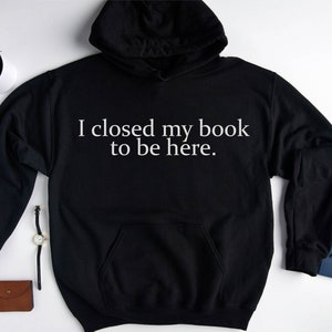 May include: Black hooded sweatshirt with white text that reads "I closed my book to be here."