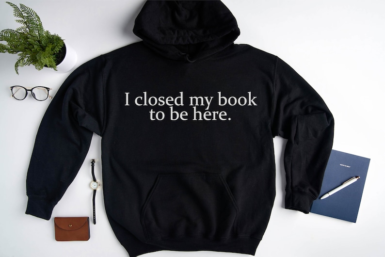 May include: Black hooded sweatshirt with white text that reads "I closed my book to be here."