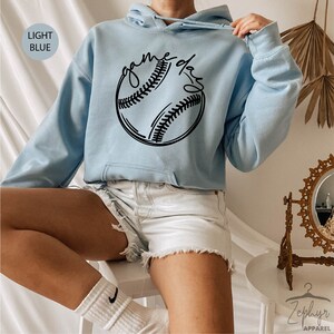 May include: Light blue hooded sweatshirt with a black baseball graphic and the text "game day" in a handwritten font.