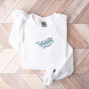 May include: White sweatshirt with a blue whale graphic and the text "all is whale" printed on the front.