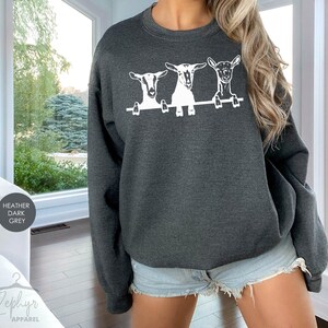May include: Heather dark grey sweatshirt with a white graphic of three goats peeking over a fence.