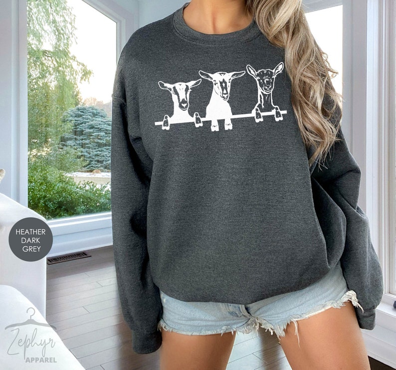 May include: Heather dark grey sweatshirt with a white graphic of three goats peeking over a fence.