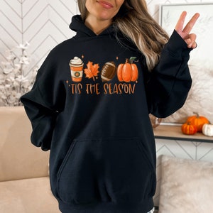 May include: Black hoodie with a graphic of a coffee cup, leaves, a football, and a pumpkin. The text "'Tis the season" is below the graphic.