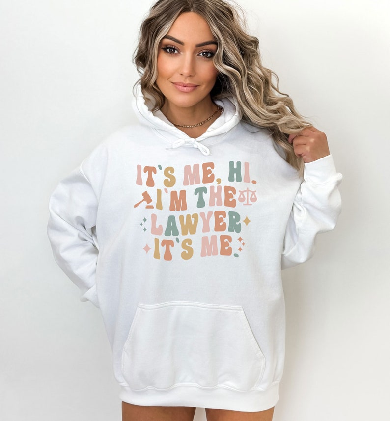 Peut inclure: Sweat-shirt &agrave; capuche blanc avec le texte "It's me, hi. I'm the lawyer. It's me." dans une police r&eacute;tro avec un graphique de marteau et de balance.