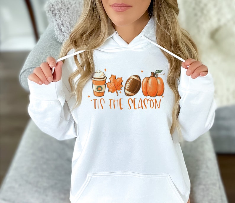 May include: White hoodie with a graphic of a coffee cup, a leaf, a football, and a pumpkin. The text "'Tis the season" is printed below the graphic.