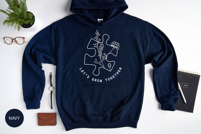 May include: Navy blue hoodie with a white outline of a puzzle piece with flowers and the text "Let's Grow Together".