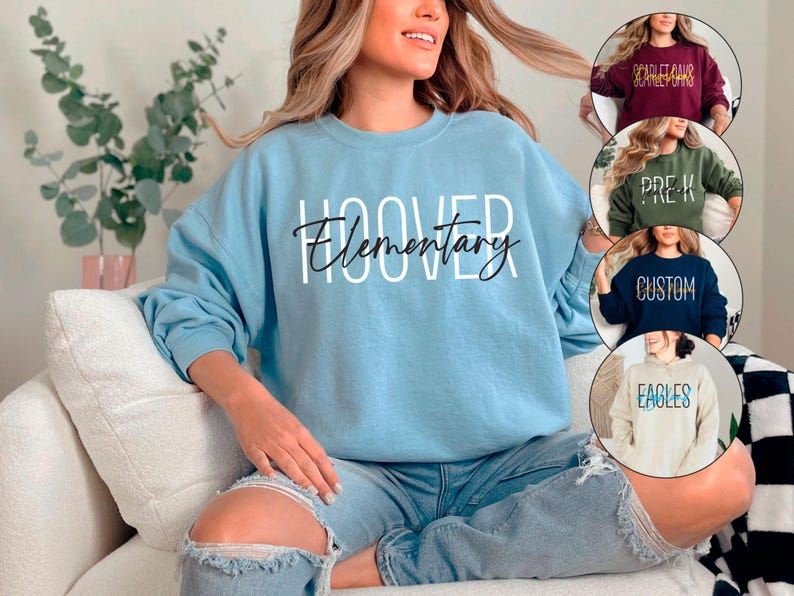 May include: A light blue sweatshirt with the text "Hoover Elementary" printed in black and white. The sweatshirt is being worn by a person sitting on a white couch.