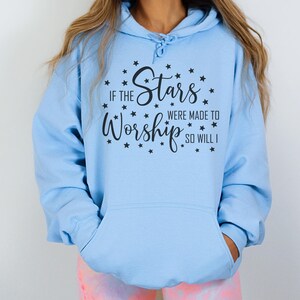 May include: Light blue hoodie with a front pocket and drawstring. The hoodie features the text "IF THE Stars WERE MADE TO Worship SO WILL I" in black script, surrounded by small black star graphics. A casual, comfortable garment.