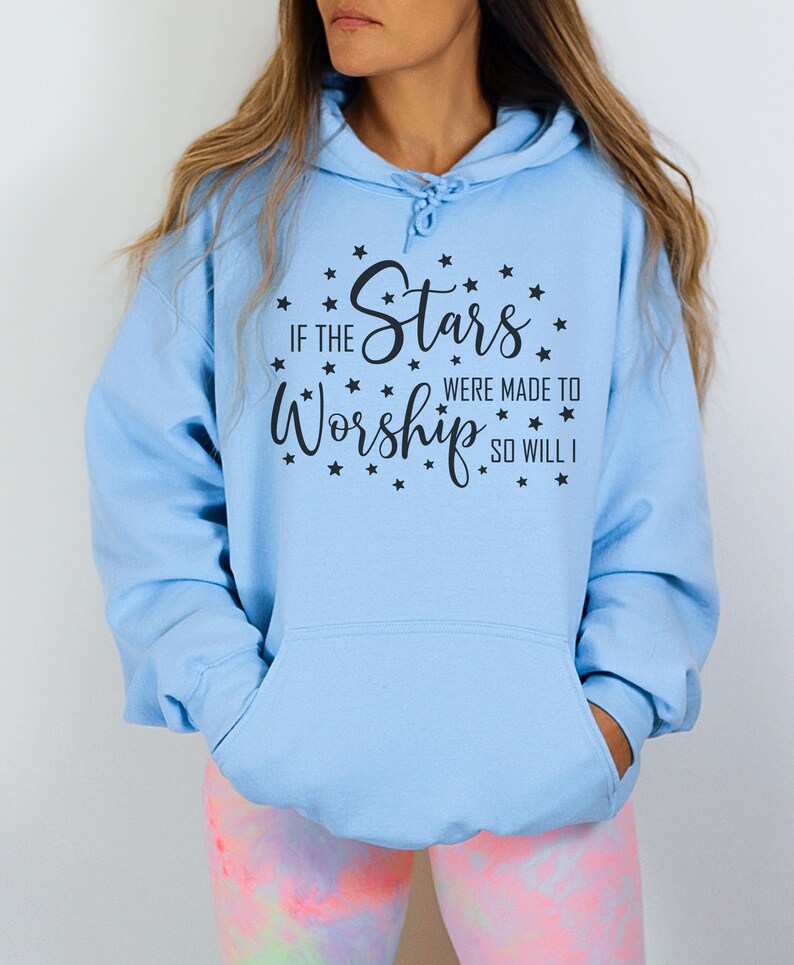 May include: Light blue hoodie with a front pocket and drawstring. The hoodie features the text "IF THE Stars WERE MADE TO Worship SO WILL I" in black script, surrounded by small black star graphics. A casual, comfortable garment.