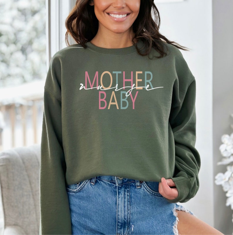 Puede incluir: Una sudadera verde con el texto "MOTHER" en rosa, azul y amarillo, y "BABY" en rosa y azul. El texto est&aacute; escrito en una fuente cursiva.