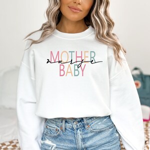Puede incluir: Sudadera blanca con el texto "MOTHER nurse BABY" en letras de colores. El texto est&aacute; en un estilo de fuente moderno.
