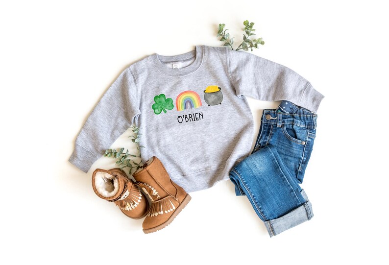May include: A gray sweatshirt with a green shamrock, rainbow, and pot of gold design. The text "O'Brien" is printed below the design.