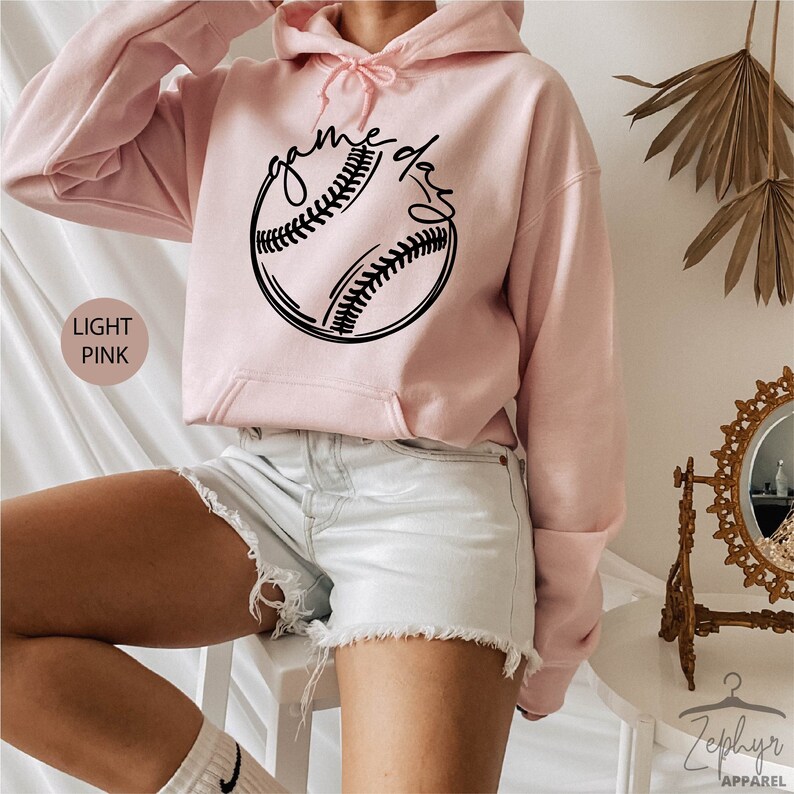 May include: A light pink hoodie with a black baseball graphic and the text "game day" on the front.