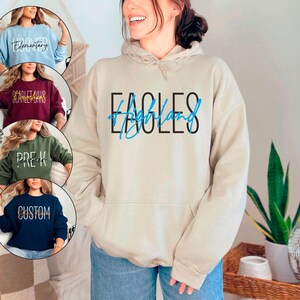 May include: A white hoodie with a blue and black graphic that says "Eagles of Highland". The hoodie has a drawstring hood and a kangaroo pocket.