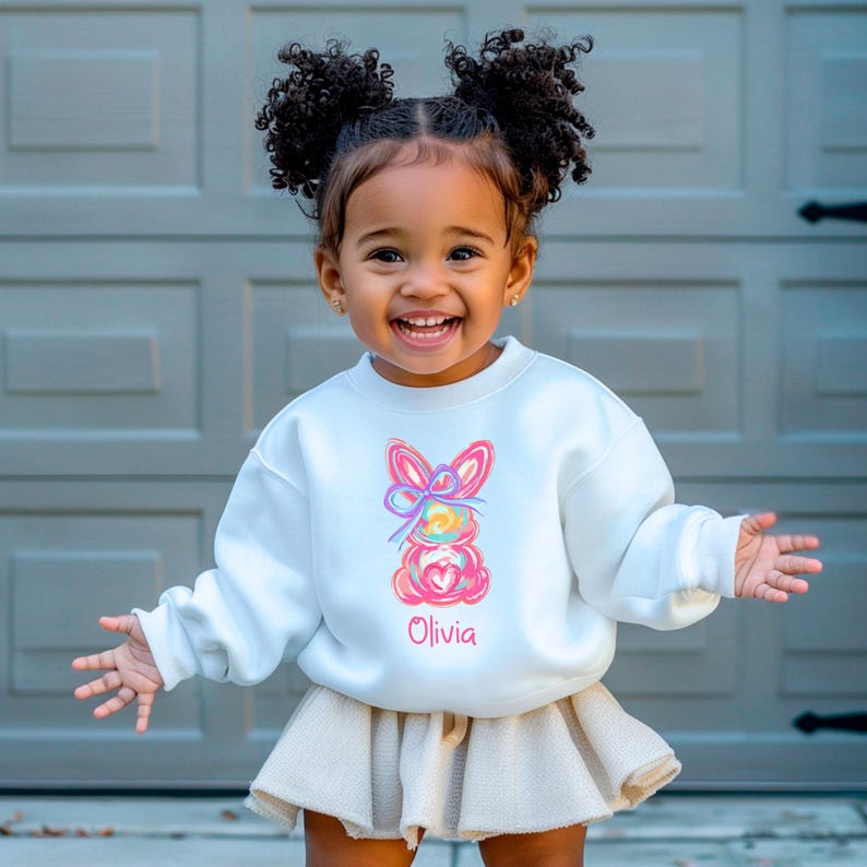 May include: White sweatshirt with a colorful Easter bunny design and the name "Olivia" embroidered on the front.