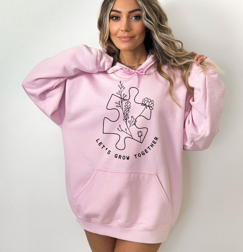 May include: A pink oversized hoodie with a black graphic of a puzzle piece with flowers and the text "Let's Grow Together".