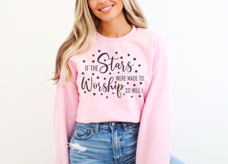 May include: A light pink sweatshirt with the text "If the Stars Were Made to Worship So Will I" in black script and star accents. The sweatshirt is paired with blue denim jeans.