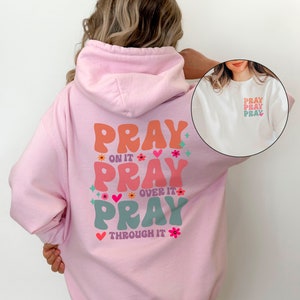 May include: Pink hoodie with a graphic on the back that says "Pray on it, Pray over it, Pray through it" in colourful, retro-style lettering with flowers and hearts.
