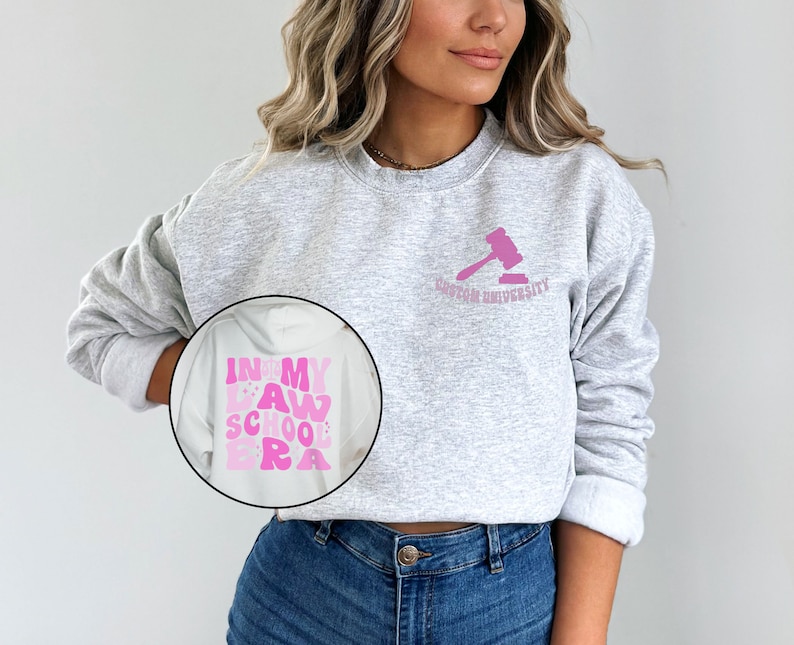 May include: A gray sweatshirt with the text "In My Law School Era" in pink letters on the left side and the text "Boston University" with a pink gavel on the right side.