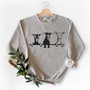 May include: A gray sweatshirt with a black graphic of three goats peeking over a fence. The goats have different facial expressions.