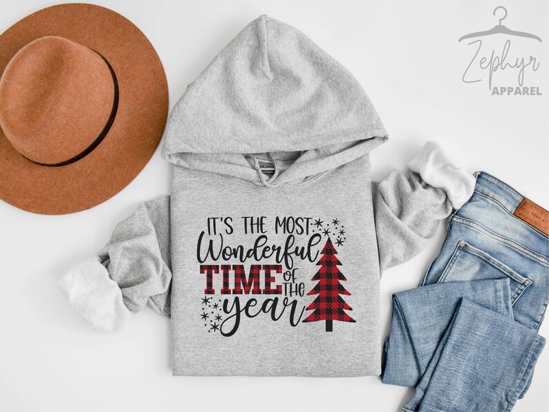Puede incluir: Sudadera gris con capucha con el texto "It's the most Wonderful Time of the year" y un gr&aacute;fico de &aacute;rbol de Navidad rojo y negro a cuadros.