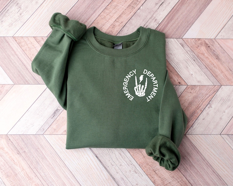 May include: A dark green sweatshirt with a white circle graphic that says "Emergency Department" with a skeleton hand making a peace sign and a lightning bolt.
