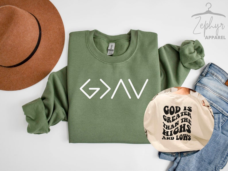以下が含まれることがあります： 白い文字で「G>A>V」と書かれた緑色のスウェットシャツ。ベージュのスウェットシャツには黒い文字で「God is greater than the highs and lows」と書かれている。