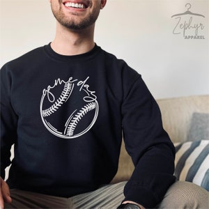 May include: Black sweatshirt with a white baseball graphic and the text "game day" written in a cursive font.