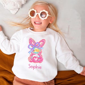 May include: White sweatshirt with a colorful abstract bunny design and the name "Sophie" printed on the front.