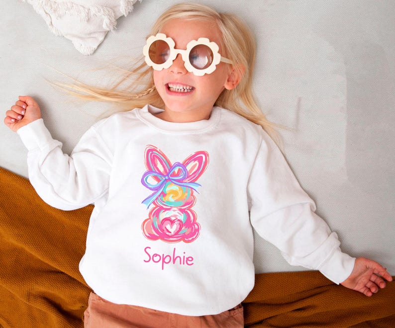 May include: White sweatshirt with a colorful abstract bunny design and the name "Sophie" printed on the front.
