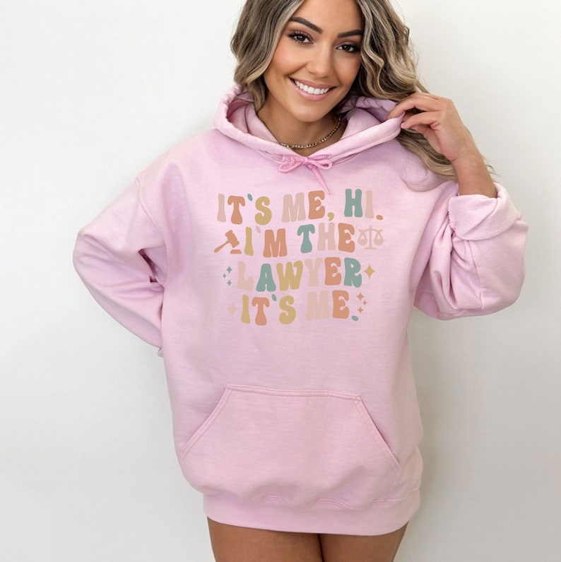 Peut inclure: Sweat-shirt &agrave; capuche rose avec un motif qui dit "C'est moi, salut. Je suis l'avocat. C'est moi." dans une police r&eacute;tro avec des accents color&eacute;s.