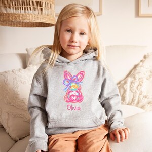 May include: A gray hoodie with a colorful bunny design and the name "Olivia" embroidered on the front.