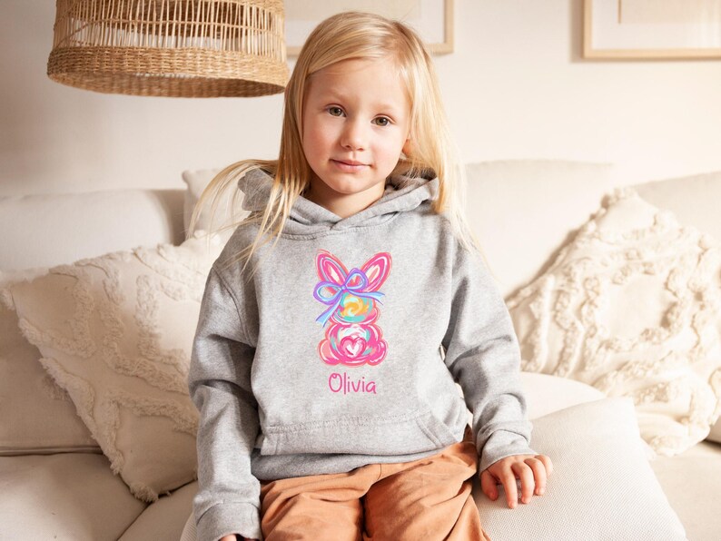 May include: A gray hoodie with a colorful bunny design and the name "Olivia" embroidered on the front.
